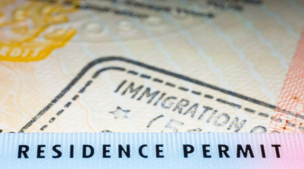 Immigration concept image. Residence permit card over immigration stamp on UK student visa in passport. Selective focus