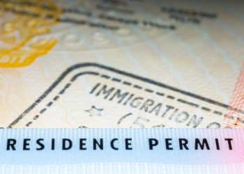 Immigration concept image. Residence permit card over immigration stamp on UK student visa in passport. Selective focus